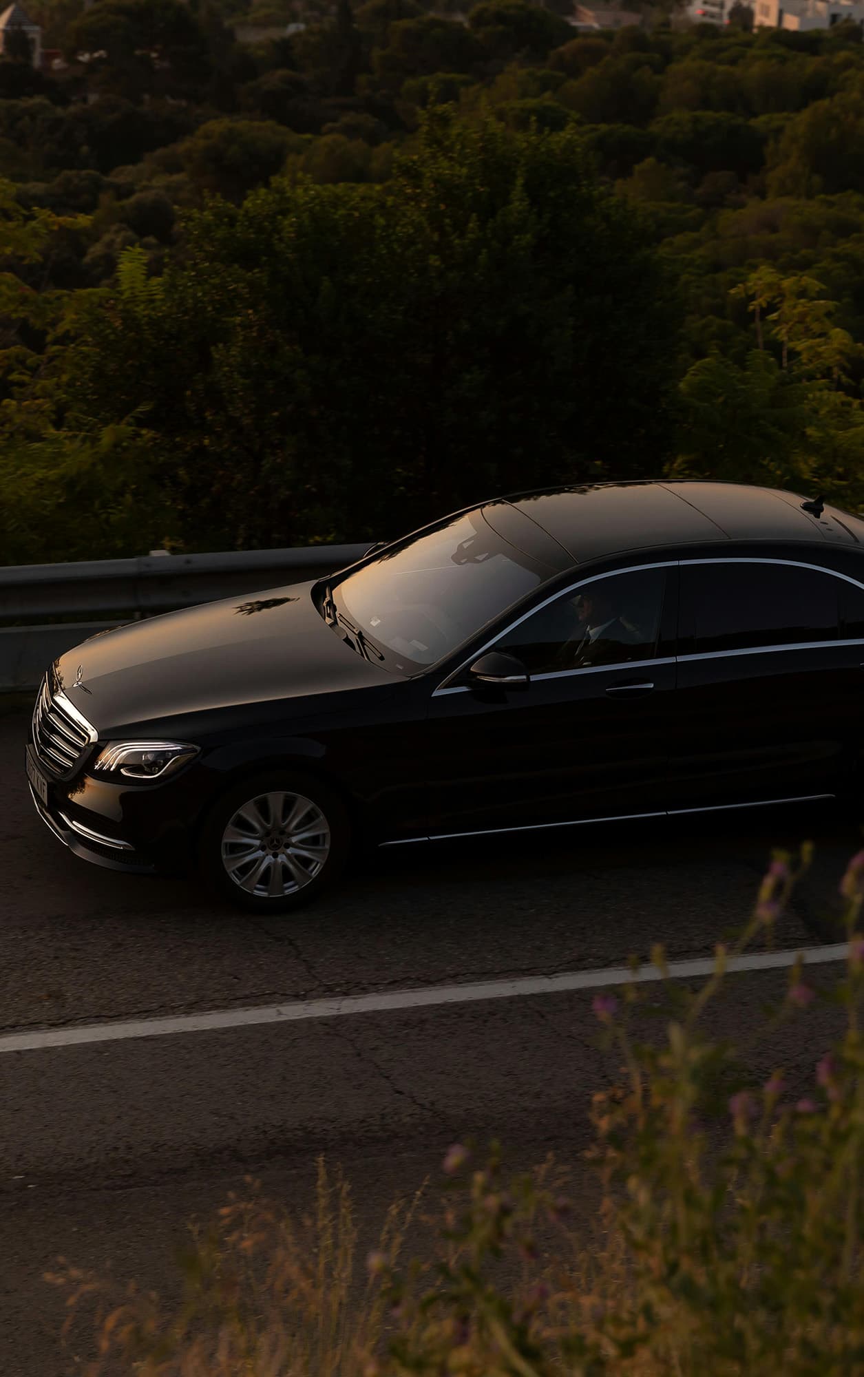 Black Mercedes luxury sedan driving on a scenic road with greenery in the background
