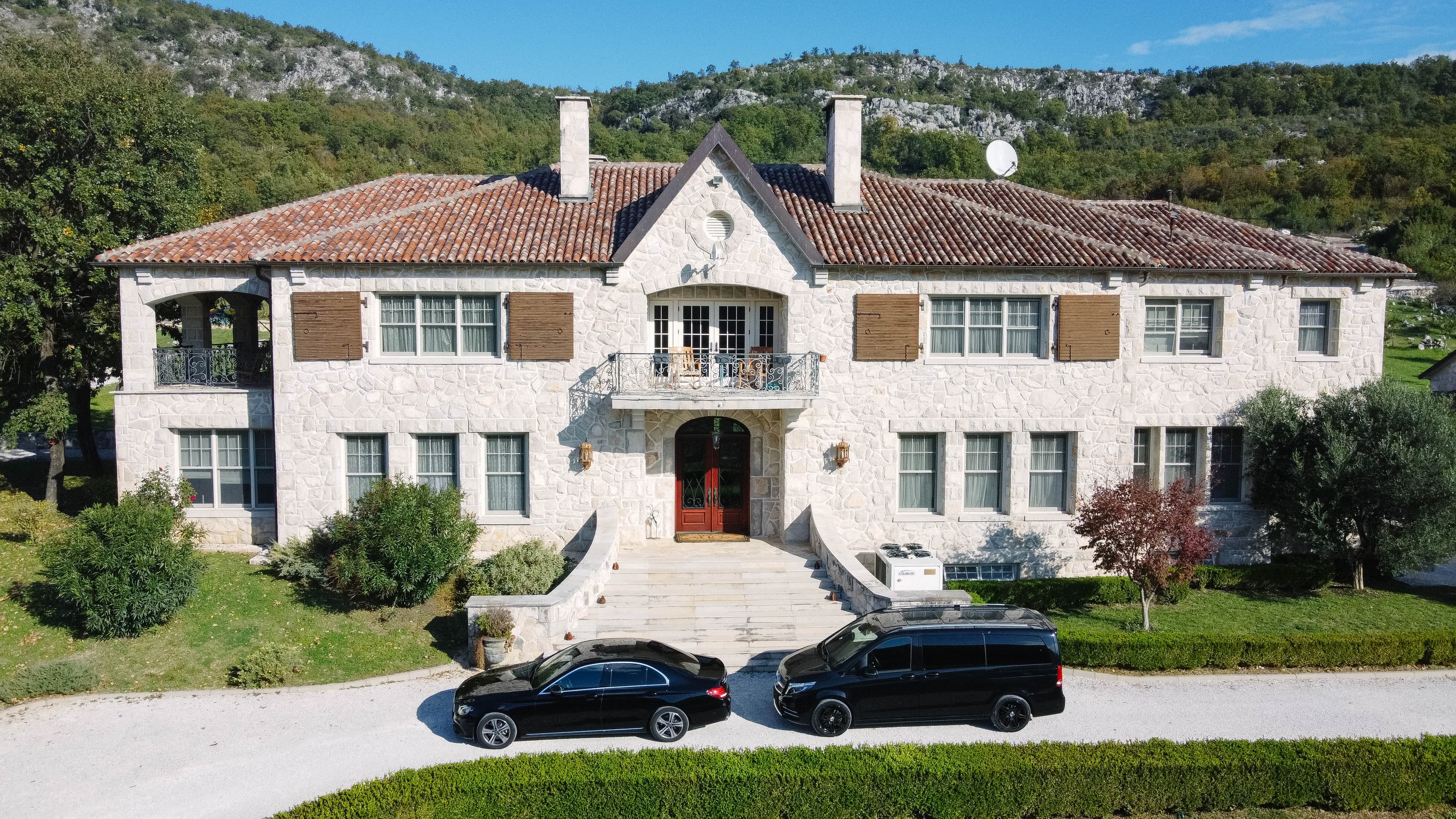 Crni Mercedes-Benz sedan i kombi parkirani ispred velike kamene kuće