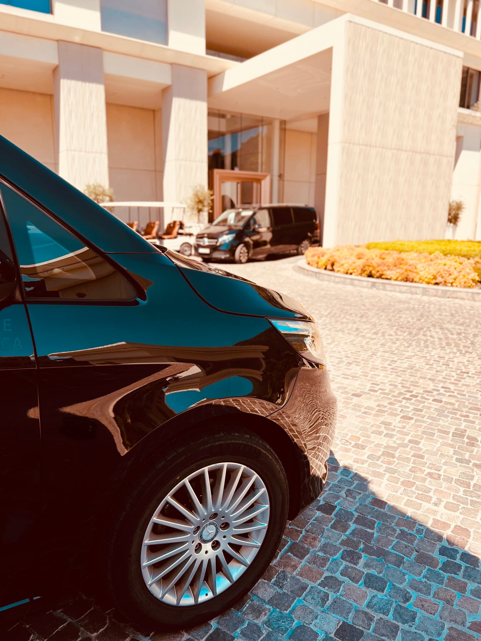 Crni Mercedes-Benz kombi parkiran ispred modernog hotelskog ulaza