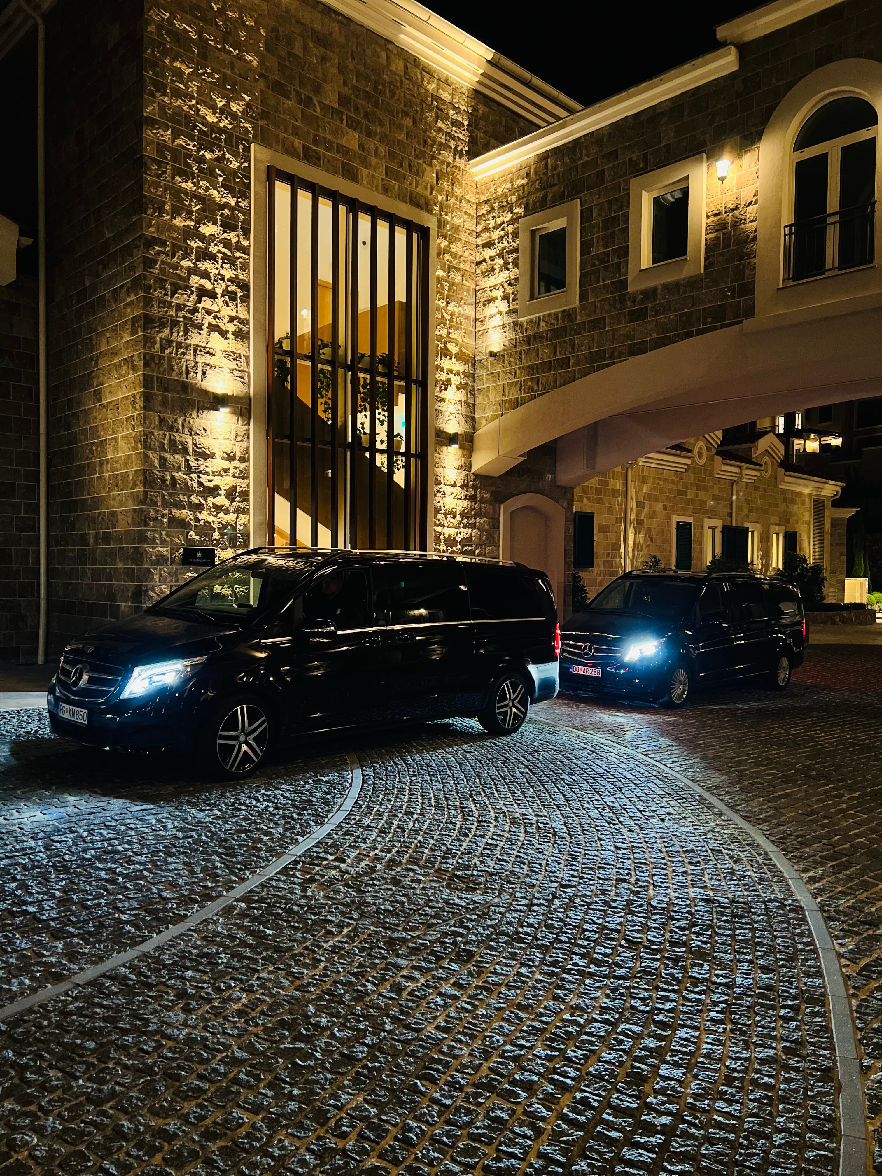 Crni Mercedes-Benz kombiji osvjetljeni svjetlima ispred kamene zgrade noću